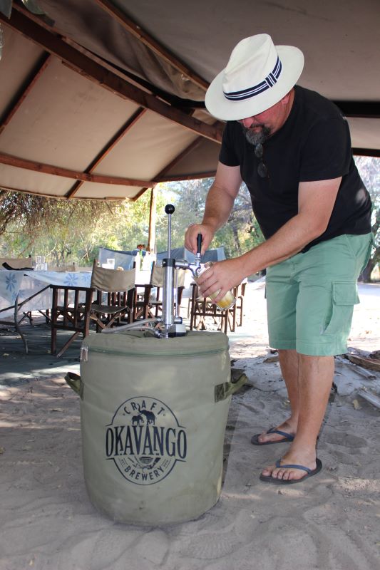a man pouring a pint of beer in a safari camp in botswana